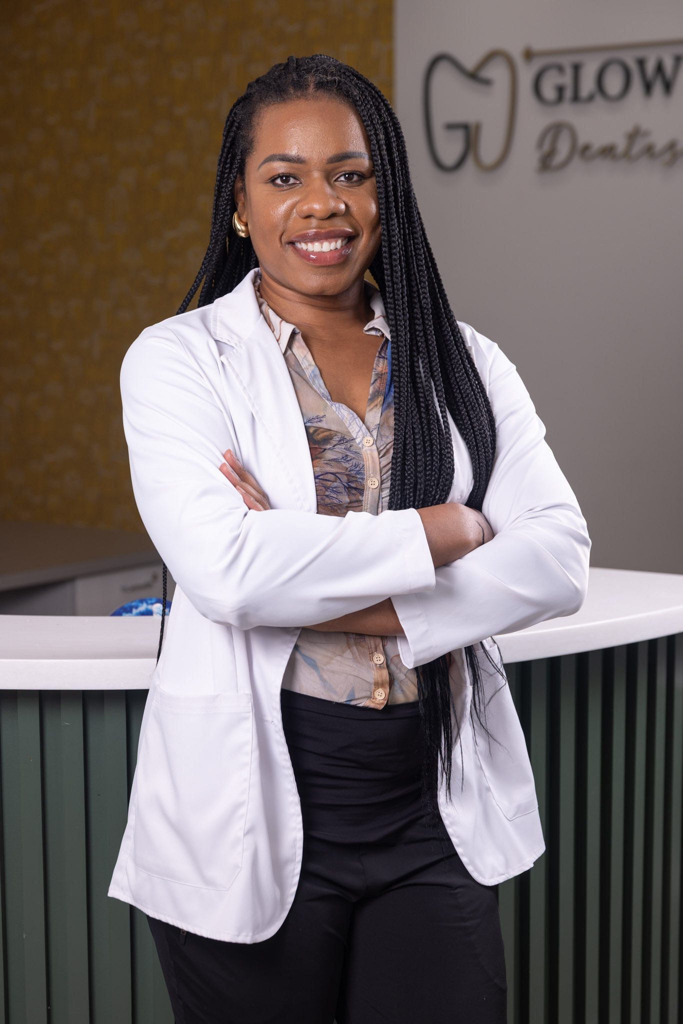 Dentist in white coat poses at reception desk in front of Glow Up Dentistry sign in Richmond, TX