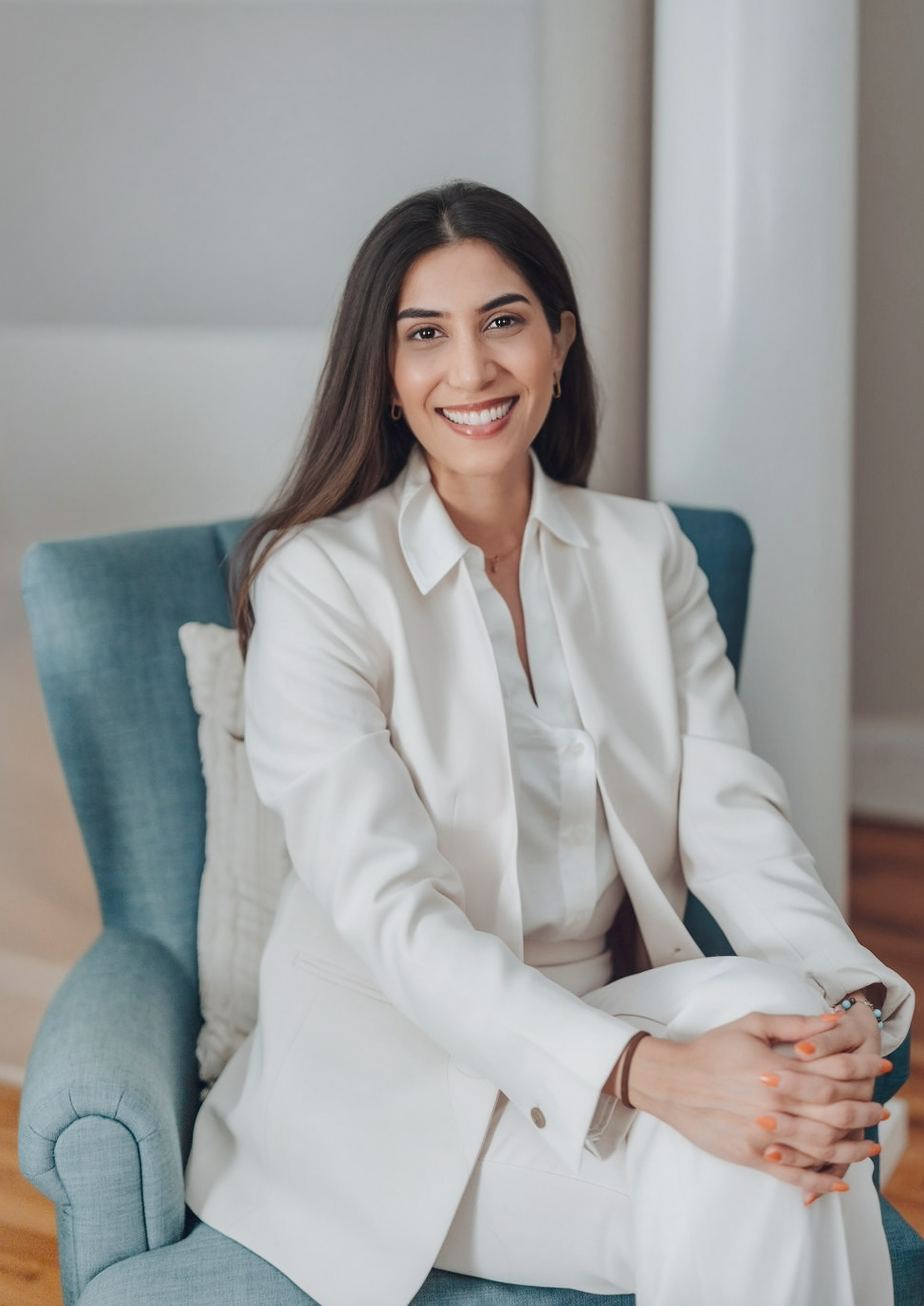 Dentist in white suit smiling while seated in a blue armchair at Dental Excellence of Brandon