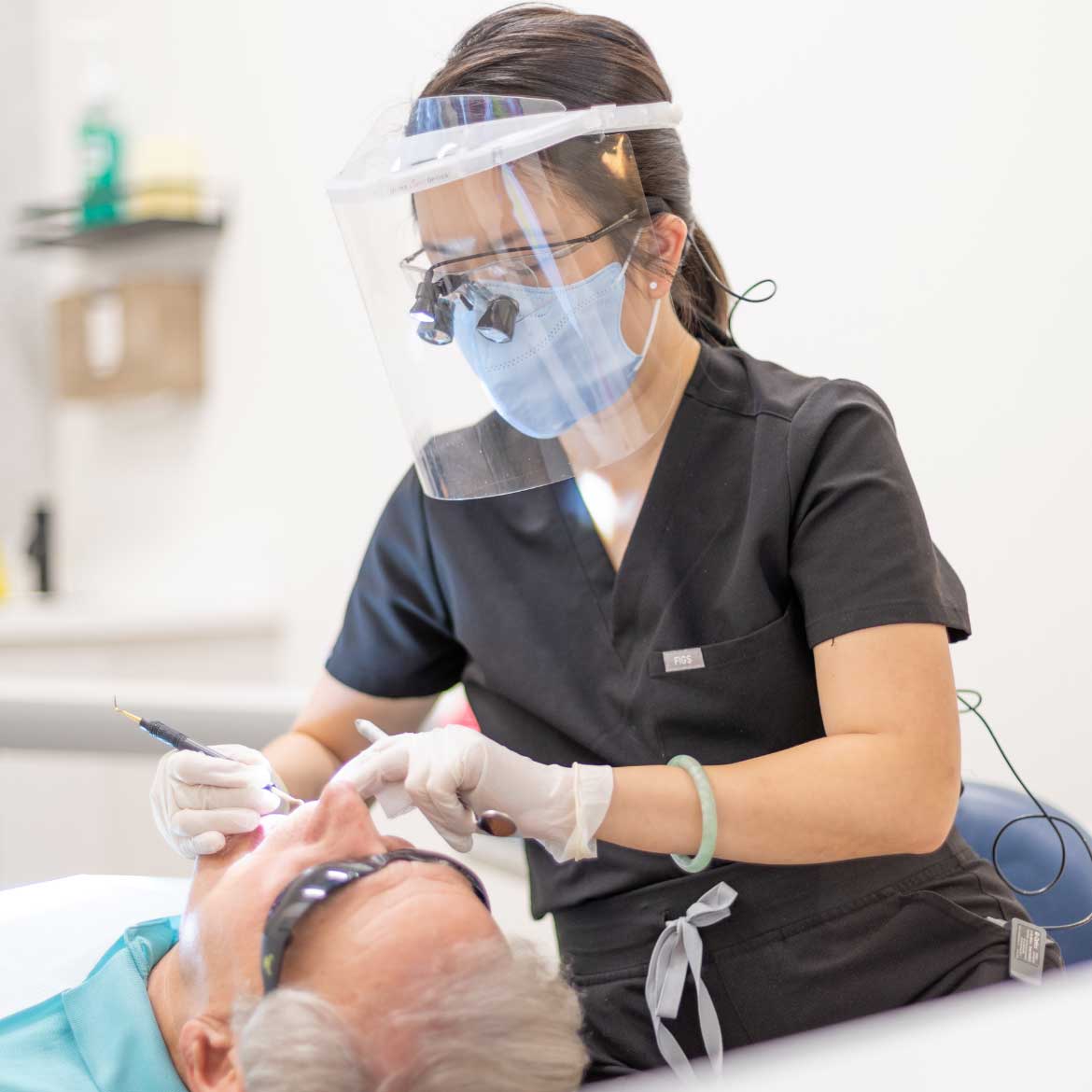 Dental hygienist wearing face shield and mask performing a procedure on a patient at Rejuvenate Dentistry
