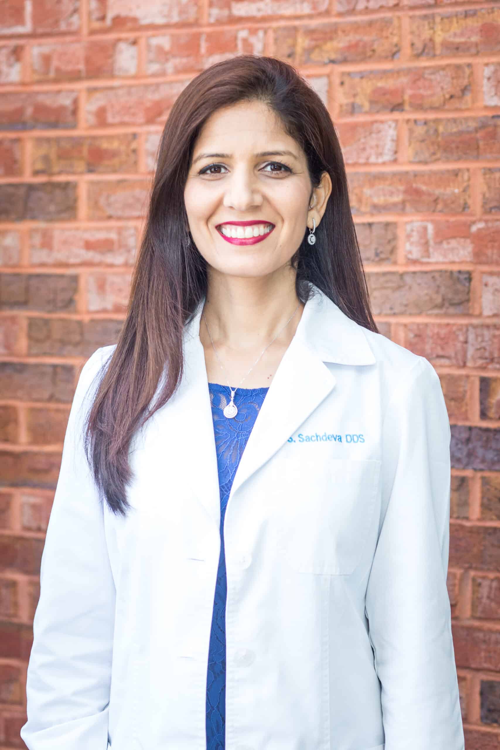Portrait of a female dentist in a white coat smiling in front of a brick wall at Sunshine Smiles Dentistry