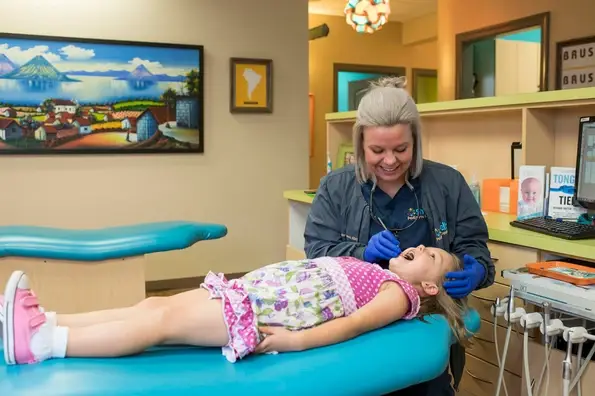 Dental hygienist examining a young girl's teeth on treatment chair at Shelby Pediatric Dentistry