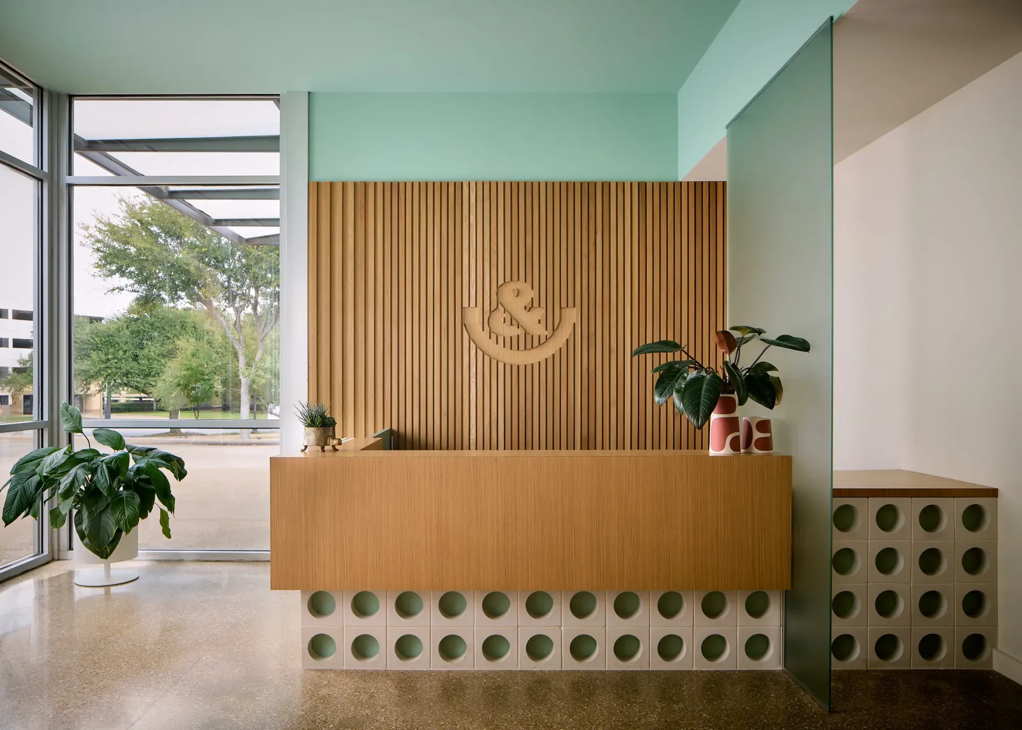 Reception counter with perforated tile base and greenery at &Smiles Pediatric Dentistry in Dallas, TX
