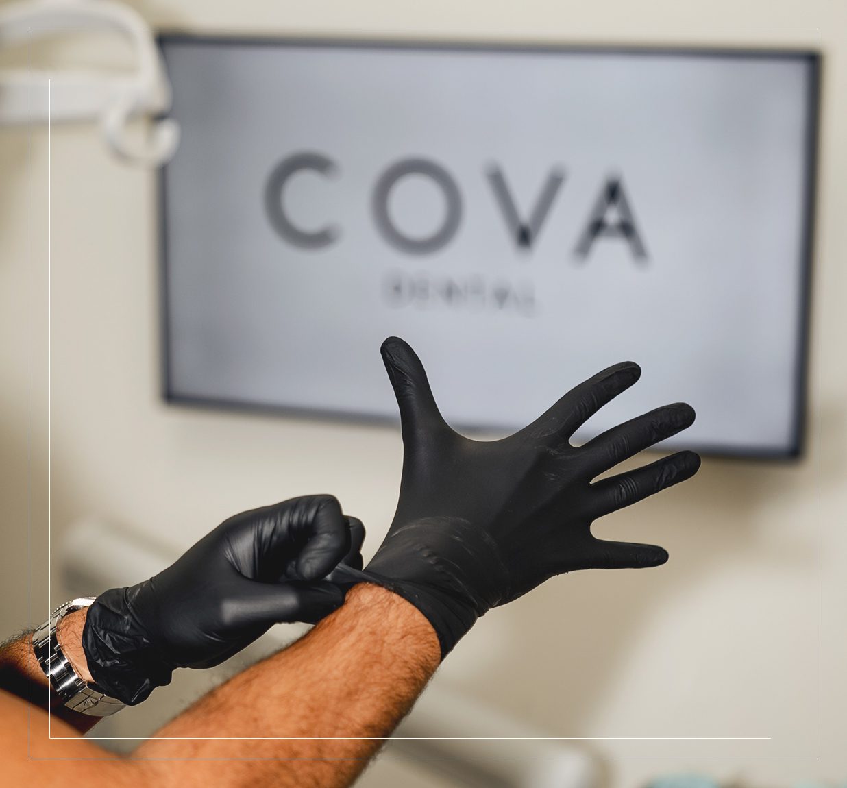 Dentist putting on black gloves in treatment room with Cova Dental logo on screen