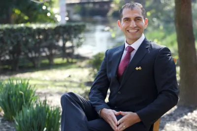 Portrait of a dentist in a suit seated outdoors near a garden at Icon Dental in Visalia, CA