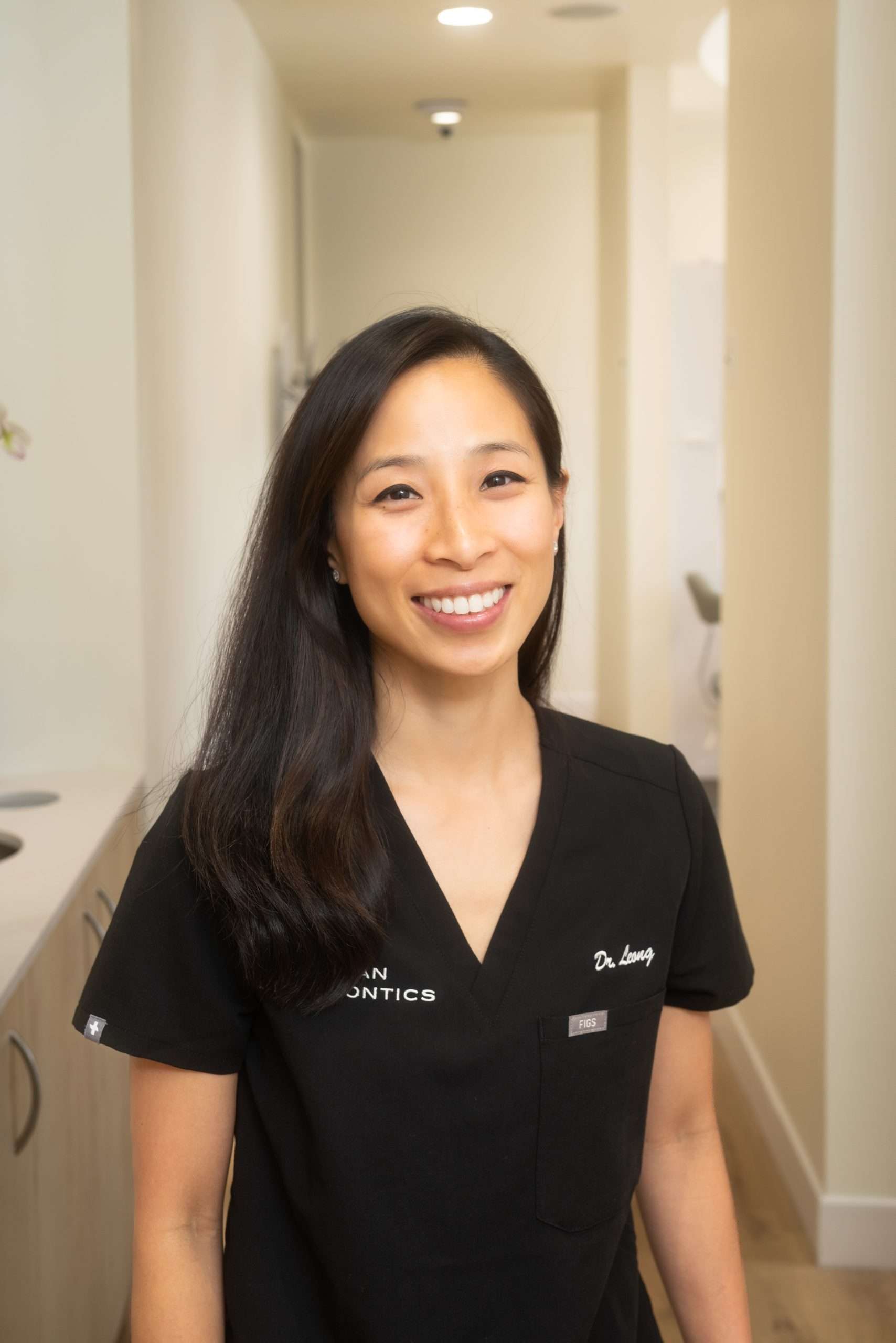 Smiling dentist in black scrubs standing in a hallway at Ocean Endodontics in San Francisco