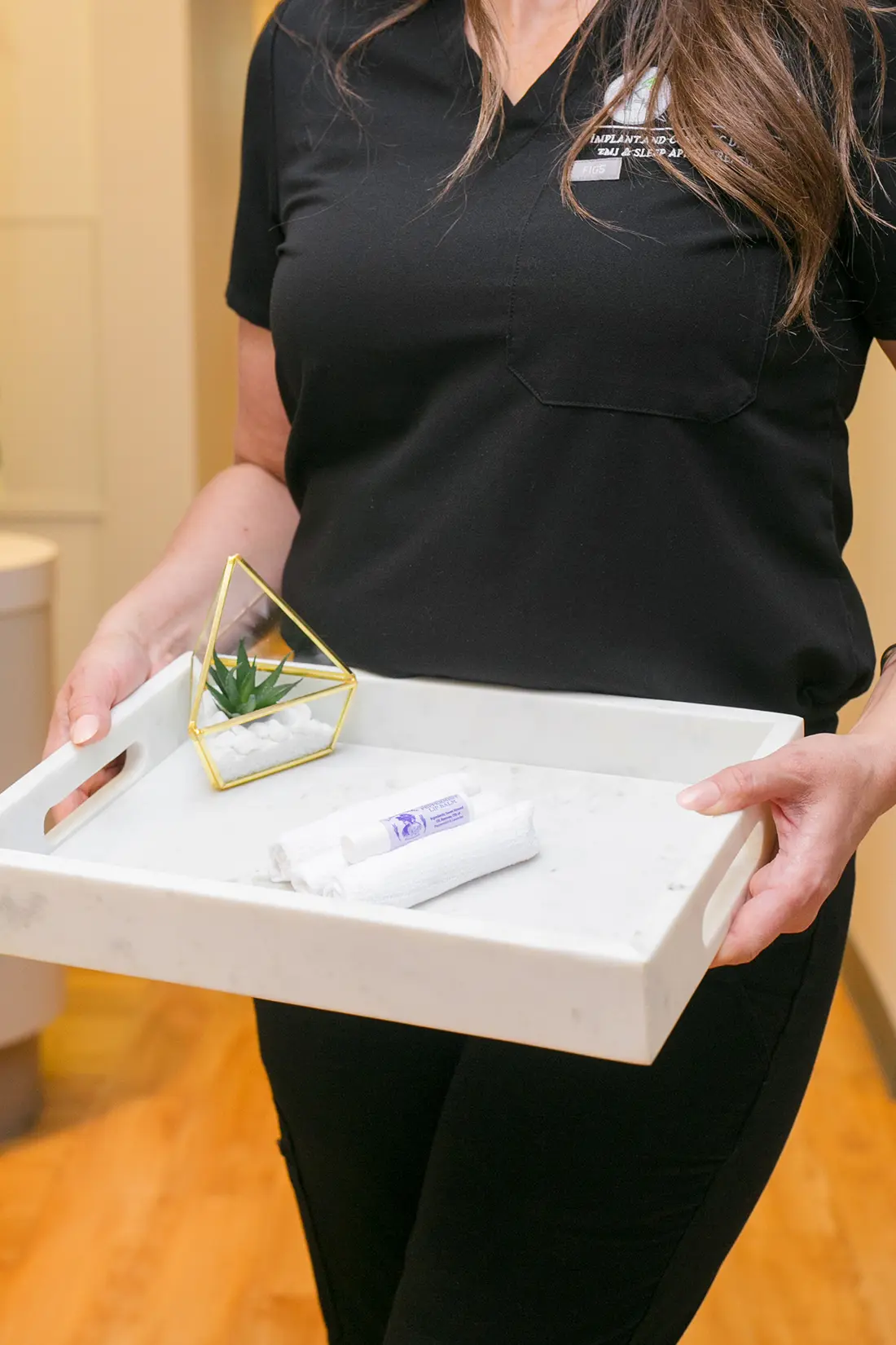 Staff member at Kinard Family Dental holding a tray with rolled towels and a small succulent