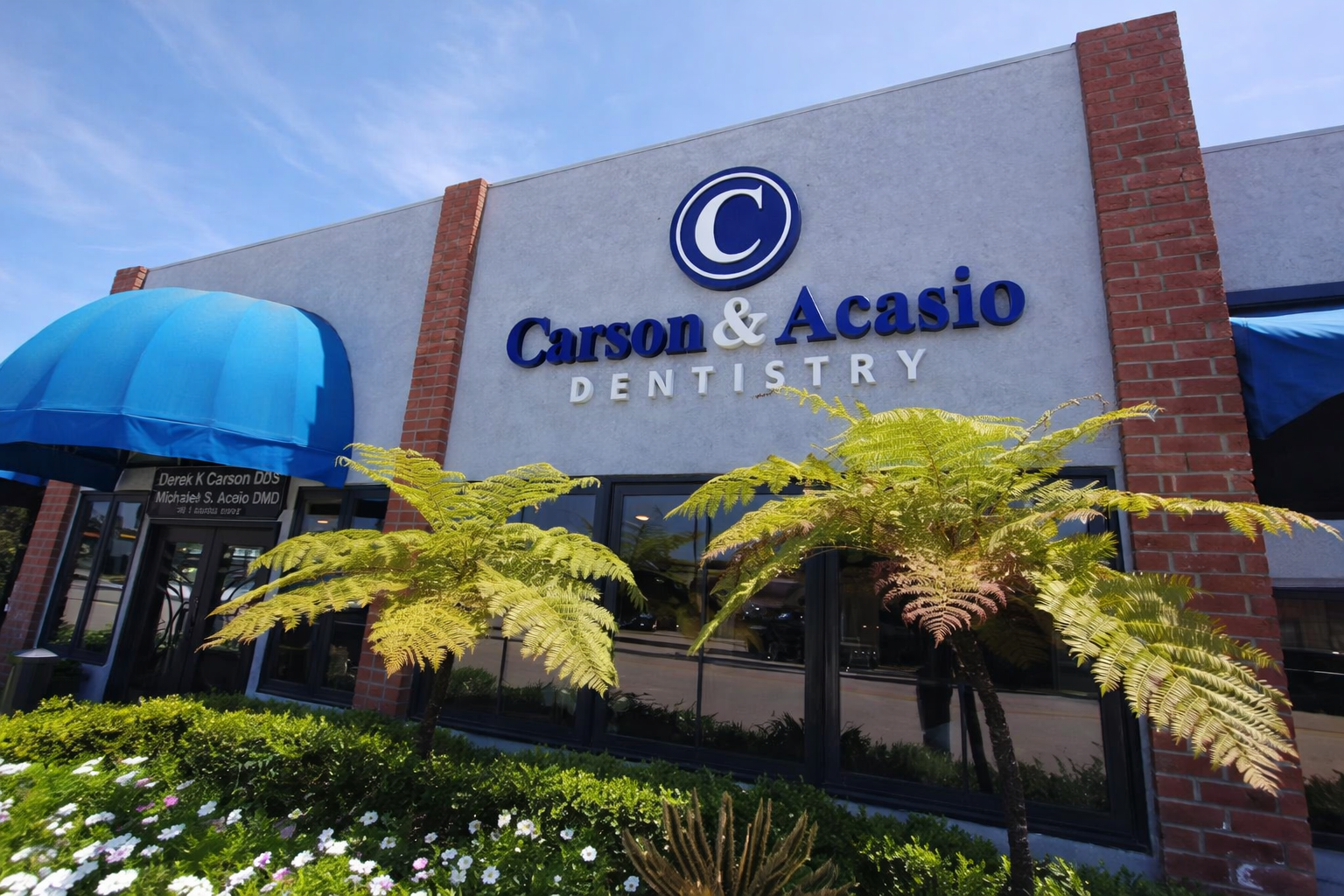 Exterior storefront sign for Carson & Acasio Dentistry in Oxnard, CA with landscaping and blue awning