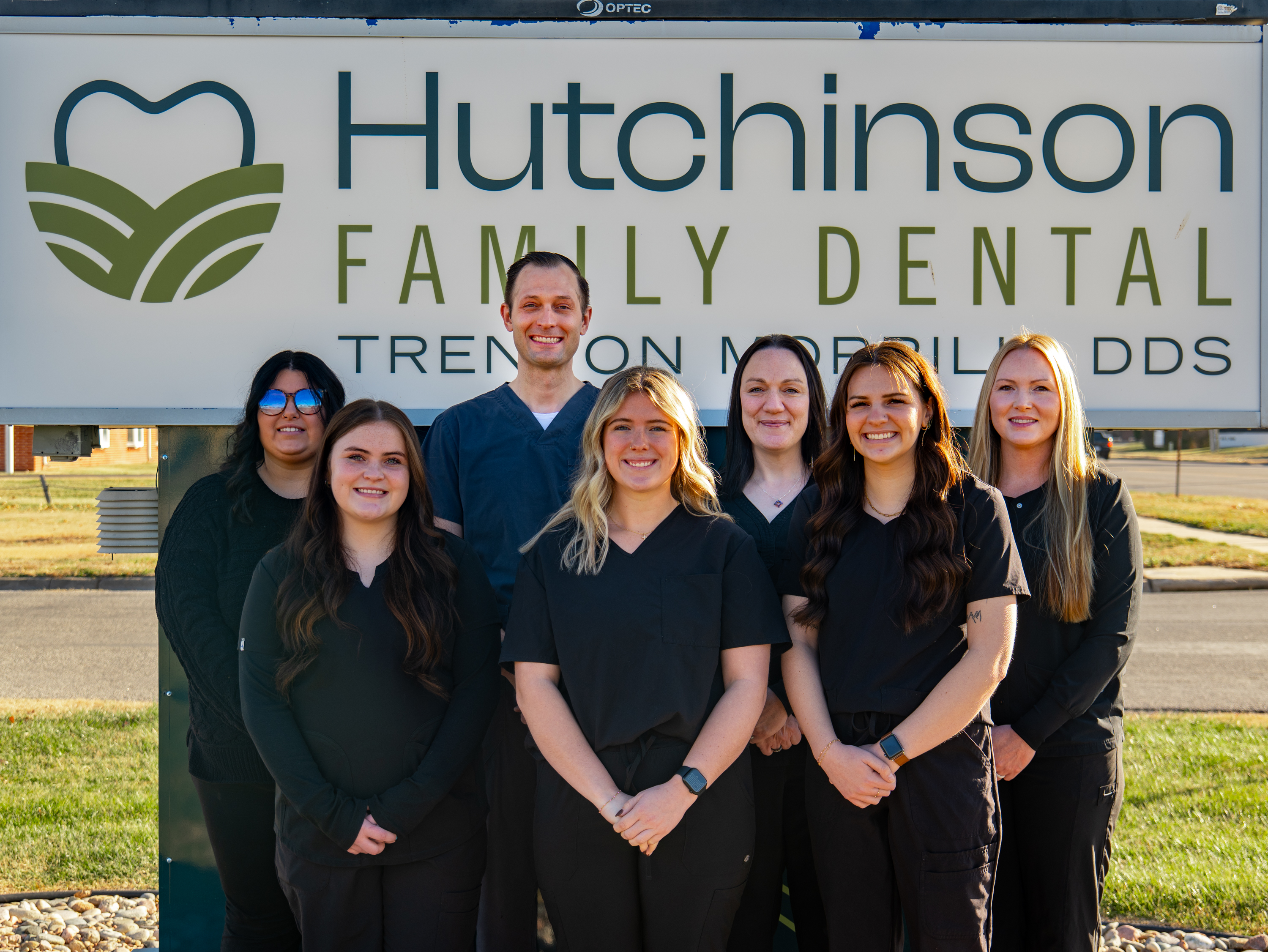 Team of Hutchinson Family Dental standing outside beneath the practice's sign in Hutchinson, KS