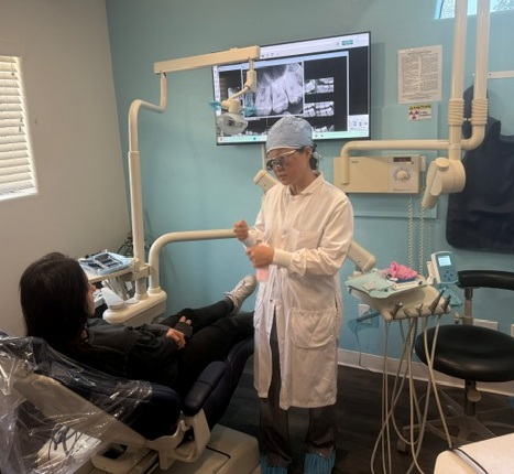 Dental staff member assisting a patient in a treatment chair with imaging displayed on monitor