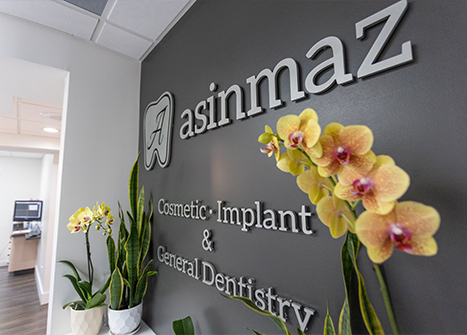 Interior sign reading 'asinmaz Cosmetic, Implant & General Dentistry' with orchids in the lobby