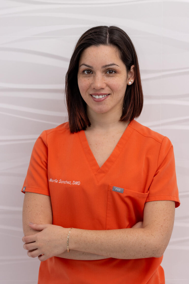 Dr. Marlie Sanchez, DMD, smiling in orange scrubs at MSG Dental in Miami Lakes