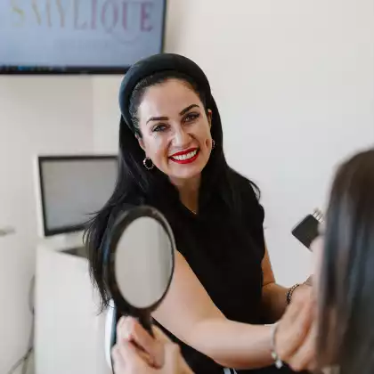 Dentist showing patient her smile in a hand mirror at Smylique Dentistry