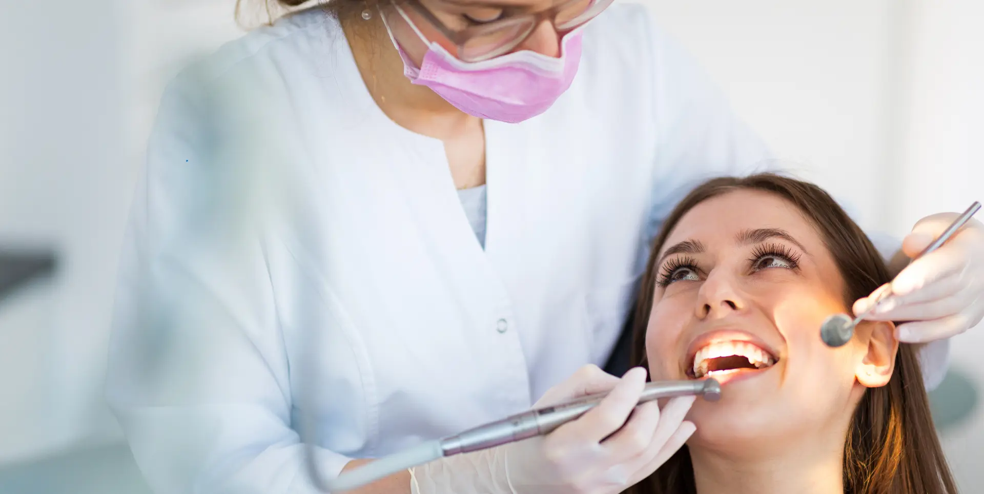 Dentist examining a smiling patient's teeth with a dental instrument at City Dental Group NYC