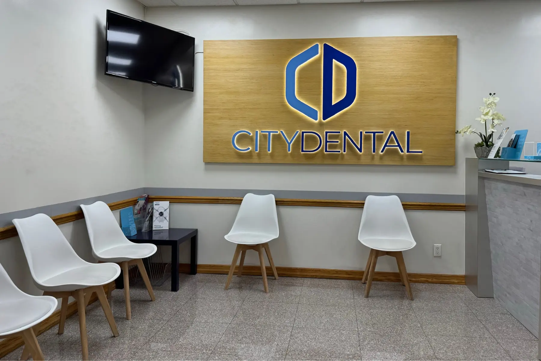 Waiting area with white chairs and illuminated City Dental logo sign at City Dental Group NYC