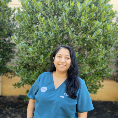 Team member in blue scrubs smiling outdoors at PRO Falls Church PLLC