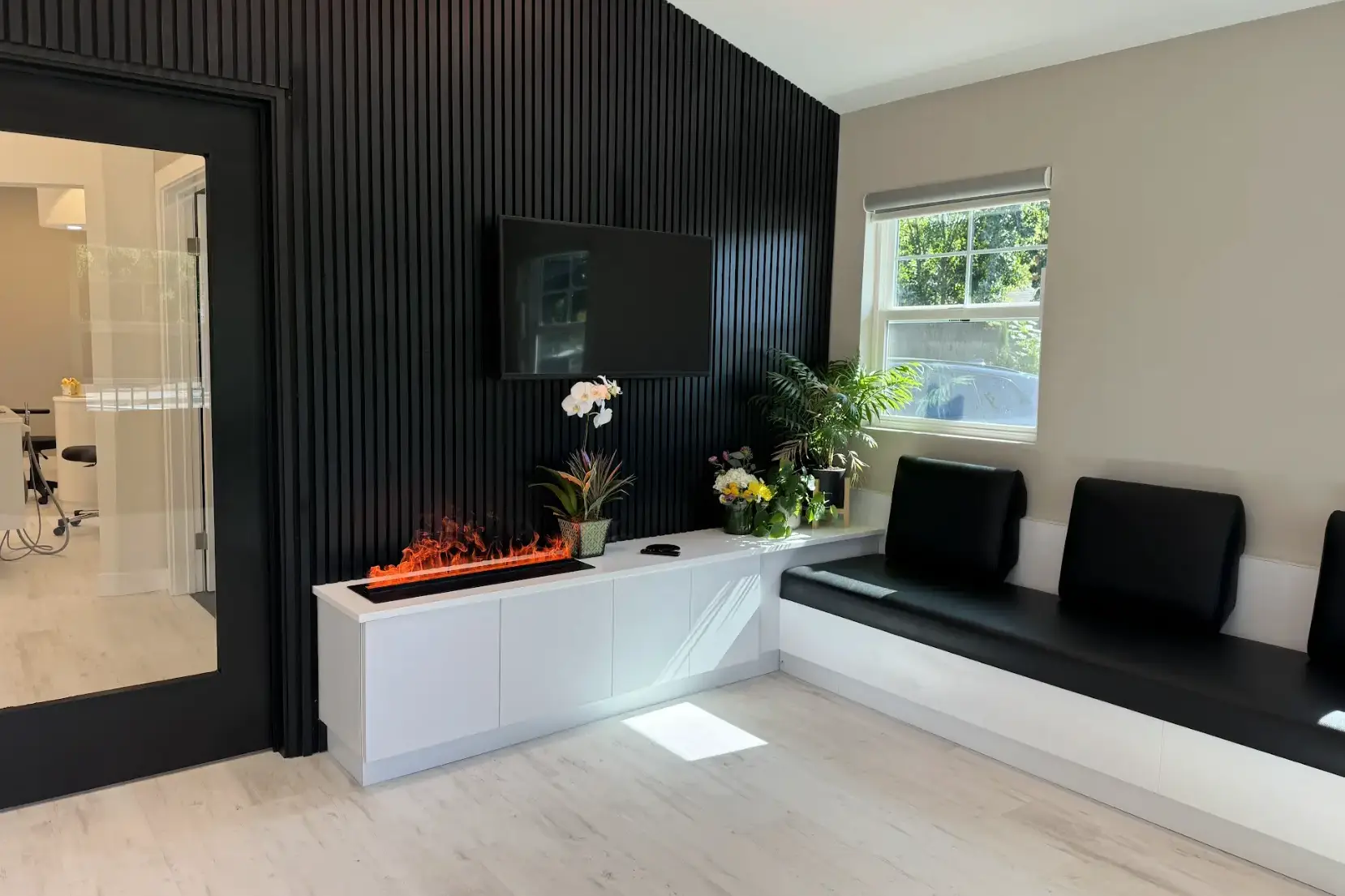 Waiting area with black slatted accent wall, fireplace feature, TV, and bench seating at Mona Lisa Smile Dental