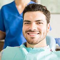 Smiling male patient in dental chair with hygienist in background at Basti Dental Care