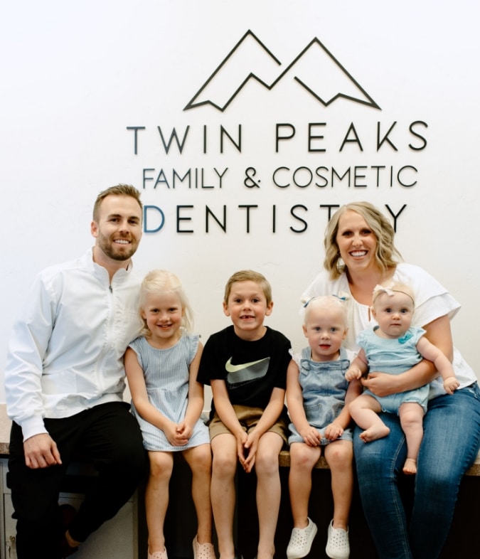 Dentist and family pose in front of Twin Peaks Family & Cosmetic Dentistry sign in Longmont, CO