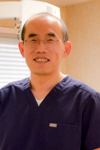 Male dentist in navy scrubs smiling in treatment room at Drexel Hill Endodontics