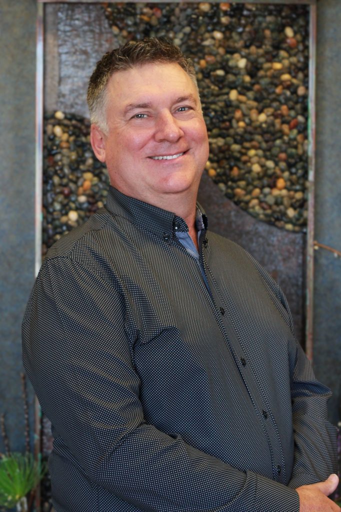 Smiling male team member at Mariah Johnson dental practice in Hudson, WI, standing by a decorative pebble wall feature.