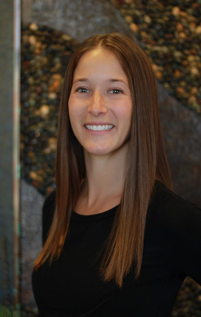 Smiling female team member at Mariah Johnson dental practice in Hudson, WI, with pebble wall background.