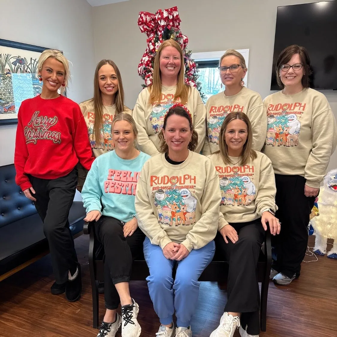 Team members at Stone Dental Clinic in Wiggins, MS posing in holiday sweatshirts by a Christmas tree