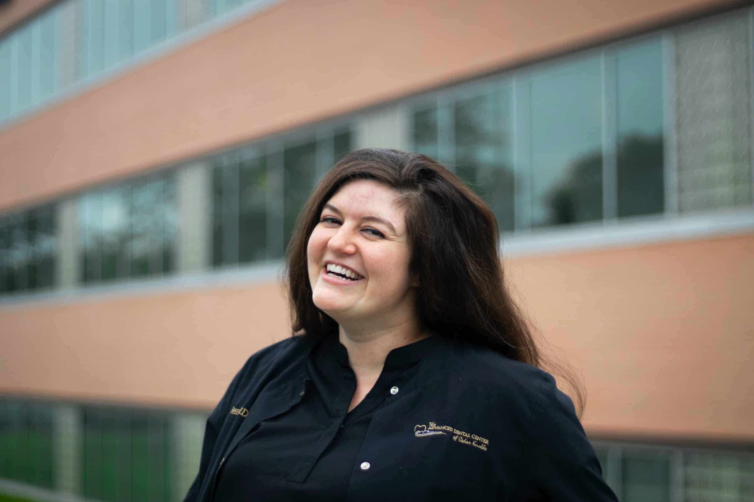 Smiling team member in black scrubs standing outside The Advanced Dental Center of Cedar Knolls
